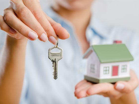 A model of a home in a hand and a woman holding a key.